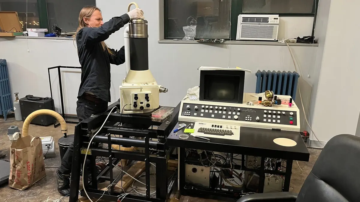 A volunteer working on a large vintage scientific instrument with a control console beside it