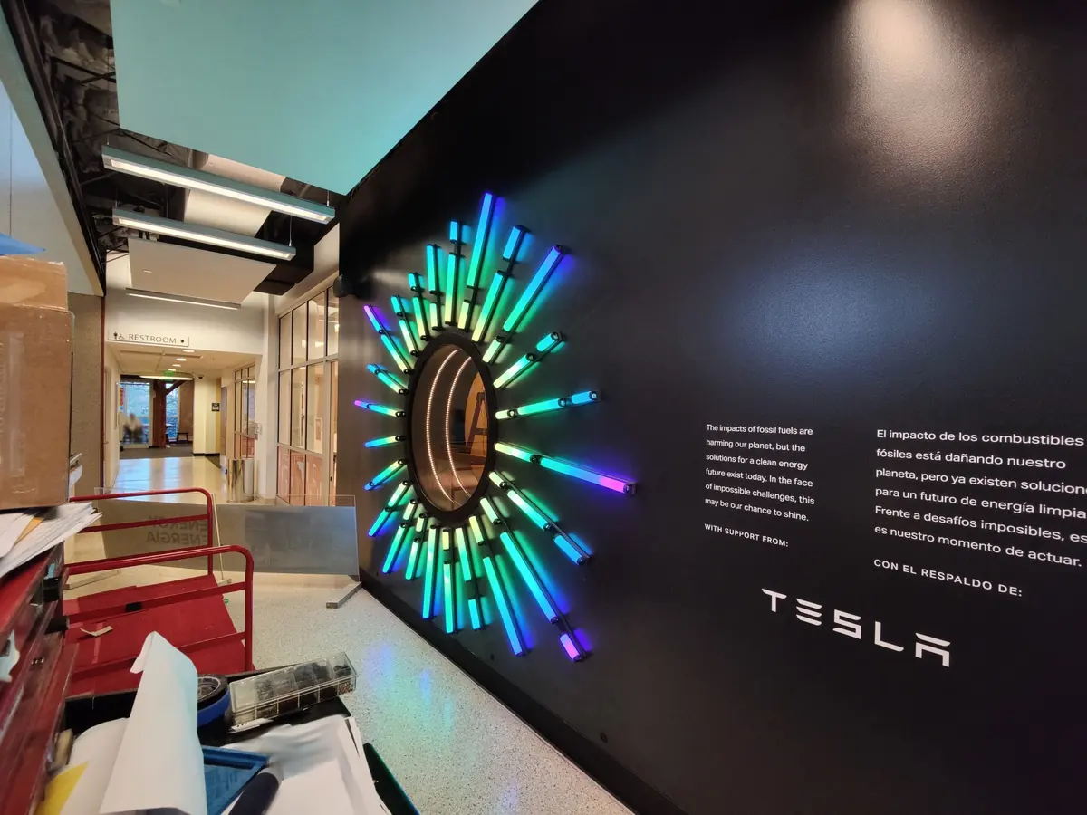 The Reactive Wall: a circular mirror ringed with colorful light tubes on a black wall