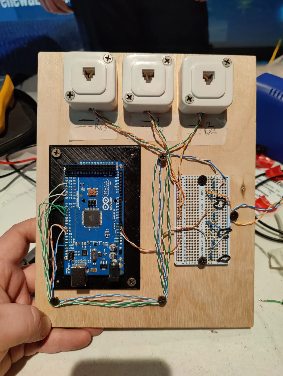 An Arduino Mega and breadboard mounted on plywood with three RJ45 jacks, held in hand