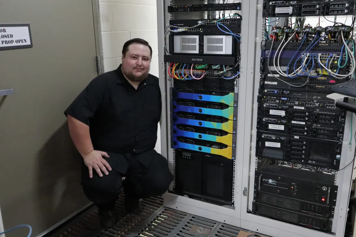 James crouching beside a network rack full of servers and switches