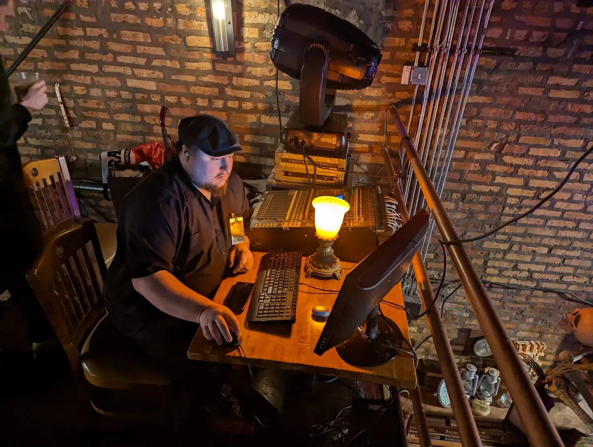 James at a desk with a computer and a lamp, in front of a brick wall
