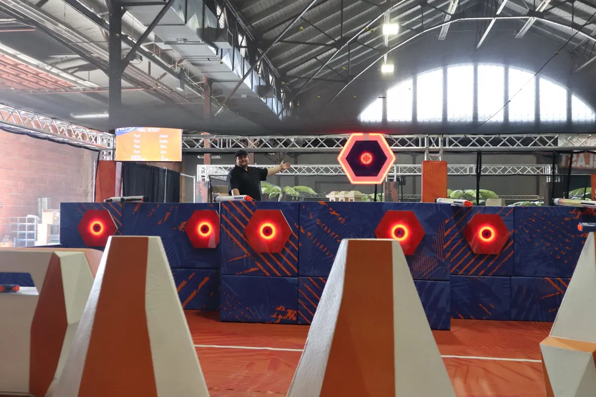 The NERF Challenge tower-defense arena: glowing hexagonal targets along a padded blue wall, behind orange barriers