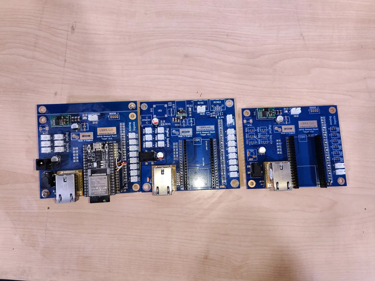 Three blue controller circuit boards laid side by side on a wooden table