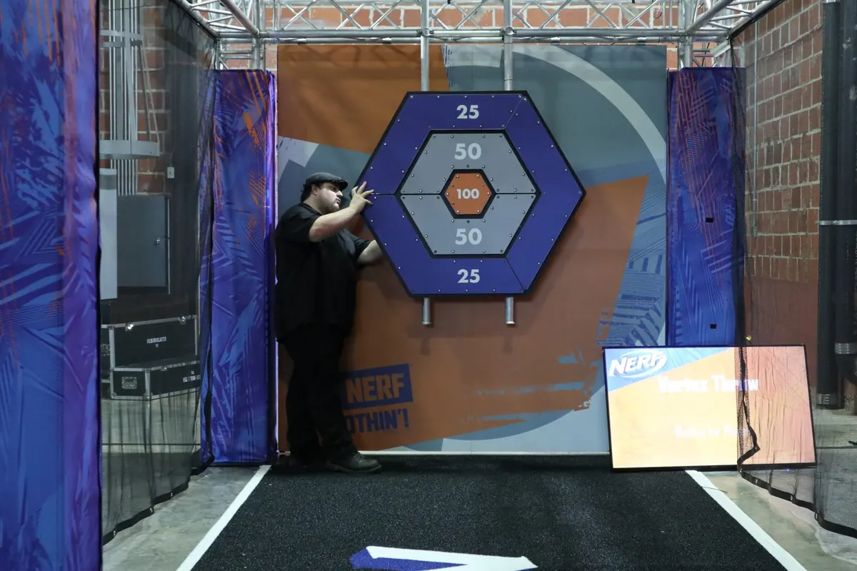 A large hexagonal target with rings scored 25, 50, and 100, framed by padded walls