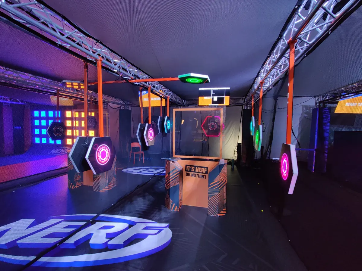 A truss-framed lane of hanging hexagonal light-up targets above a large NERF floor logo