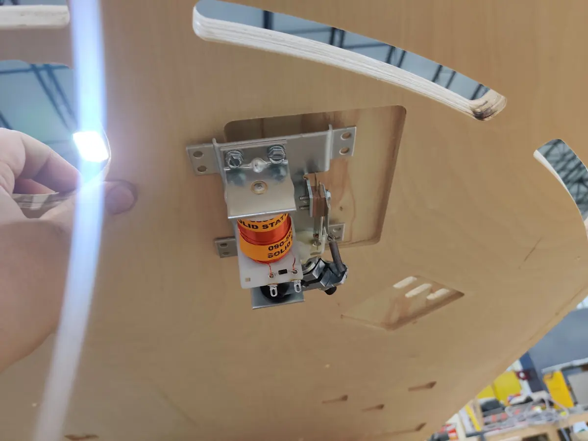 A flipper mechanism mounted in a cutout on the wrong side of the plywood playfield